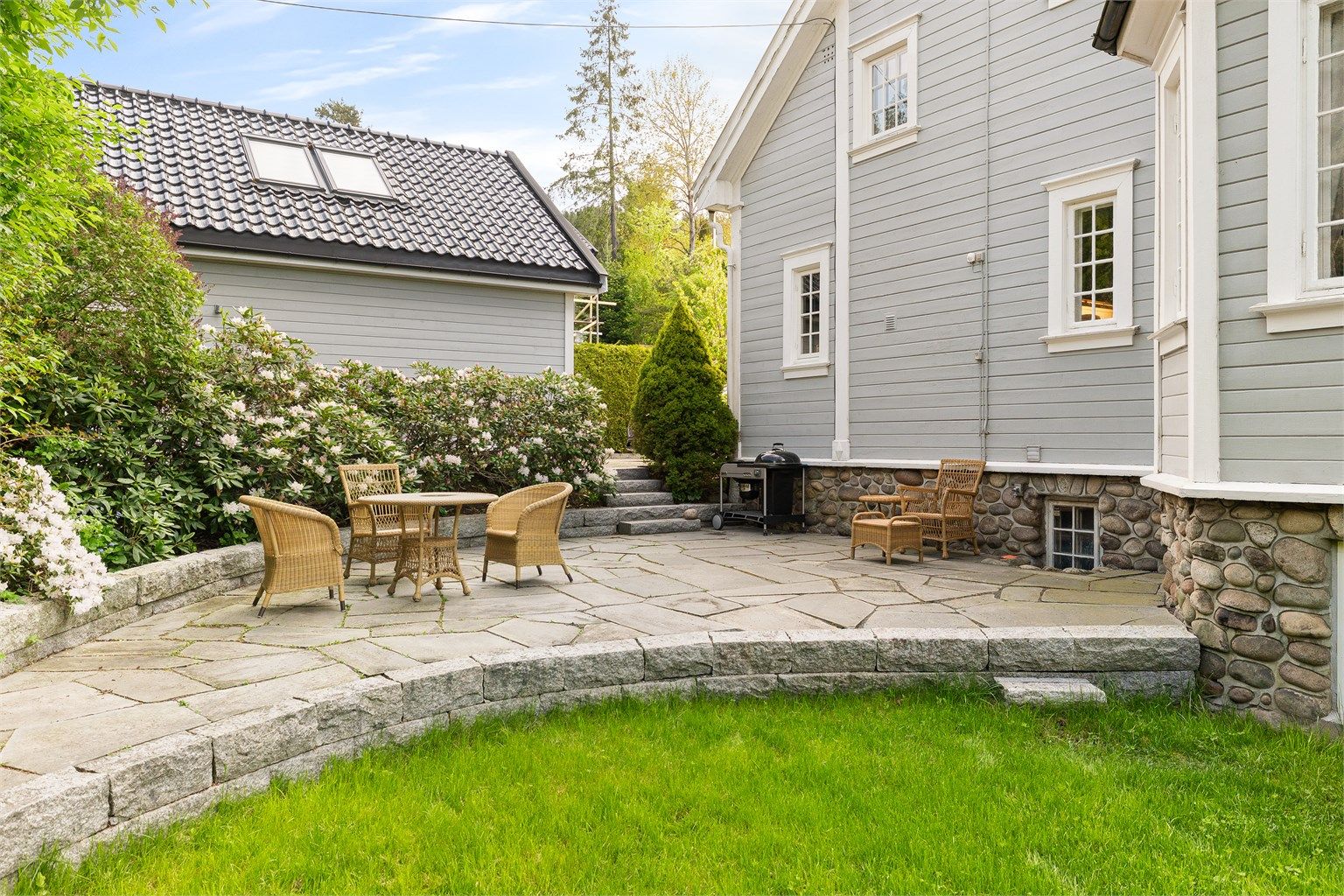 Uteplass med god plass til sittegruppe, omkranset av plen og beplantning.