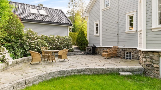 Uteplass med god plass til sittegruppe, omkranset av plen og beplantning.