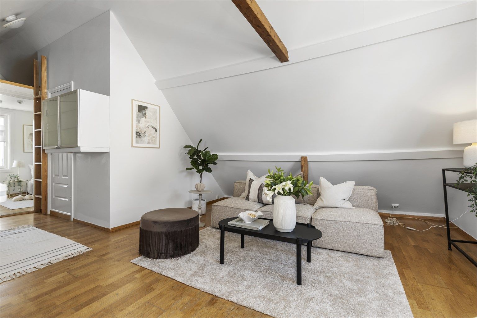 Loftstuen har hyggelig skråtak, synlige bjelker og parkett på gulv.