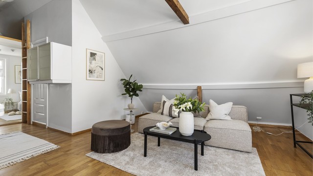 Loftstuen har hyggelig skråtak, synlige bjelker og parkett på gulv.