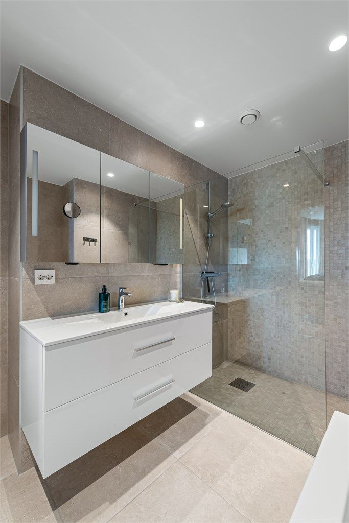 Baderomsinnredning med skuffer og servant med ett-greps armatur. Speilskap og stikkontakt over servant. Dusjhjørne med glassvegg og vegghengt dusjarmatur. Spotter i tak