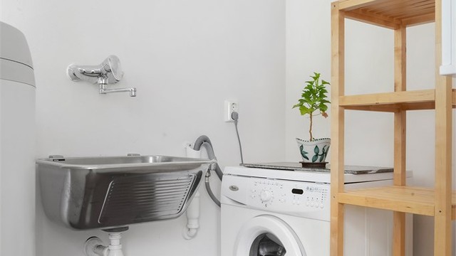 Praktisk vaskerom med gulvbelegg, utslagsvask og opplegg for vaskemaskin.