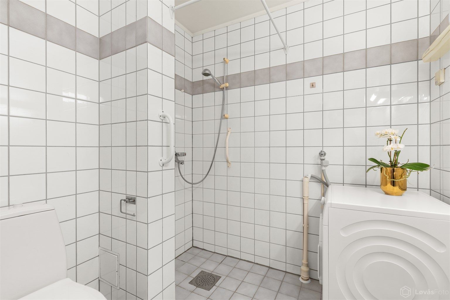 Badet inneholder dusjhjørne, vegghengt servant og toalett. 