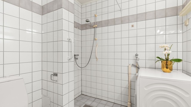 Badet inneholder dusjhjørne, vegghengt servant og toalett.
