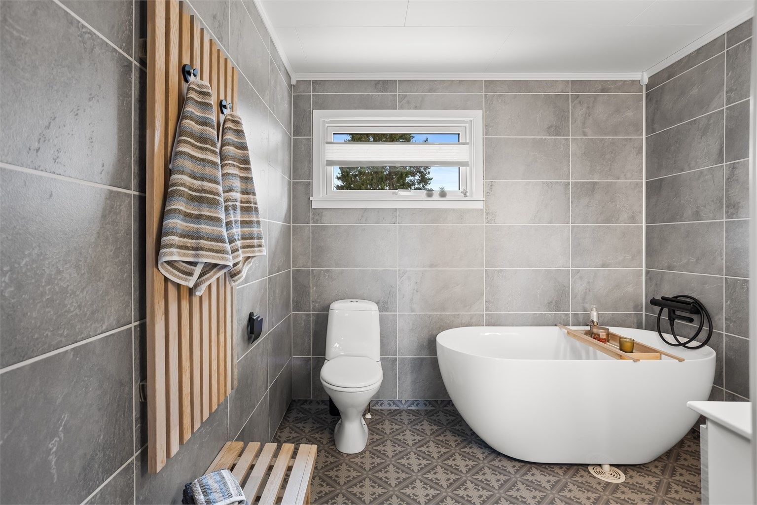 Baderommet er innredet med badekar, vegghengt servantskap med heldekkende servant og høyskap.