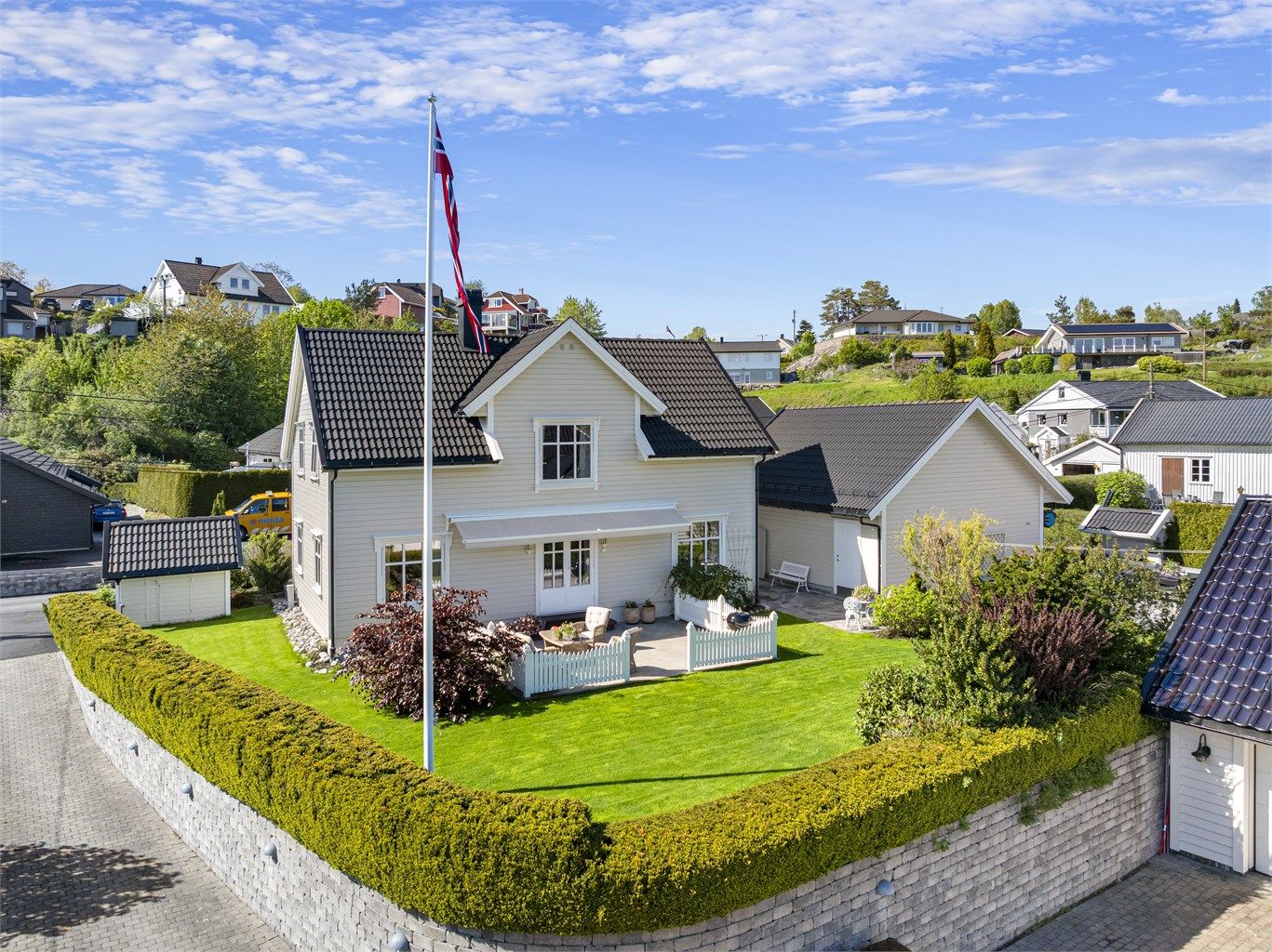 Eiendommen er pent plassert på en tilnærmet flat tomt, opparbeidet med plen og hekk.