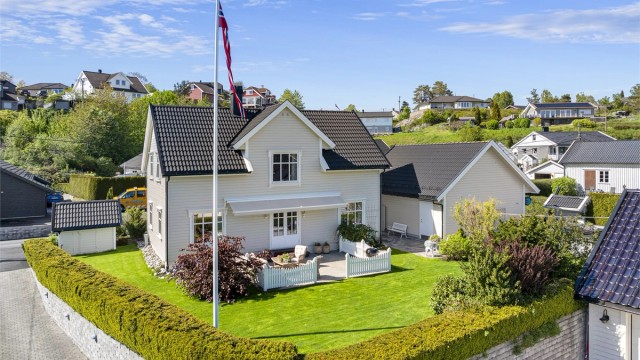 Eiendommen er pent plassert på en tilnærmet flat tomt, opparbeidet med plen og hekk.