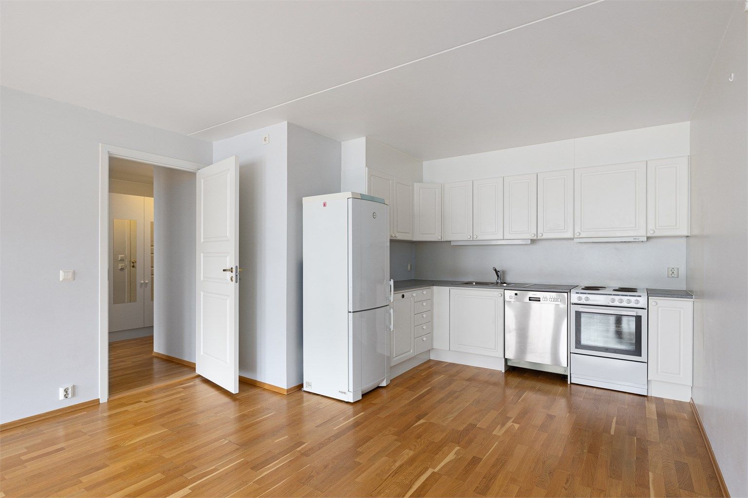 Moderne løsning med åpen kjøkkenløsning. Kjøkkeninnredning fra byggeår med profilerte hvite fronter.