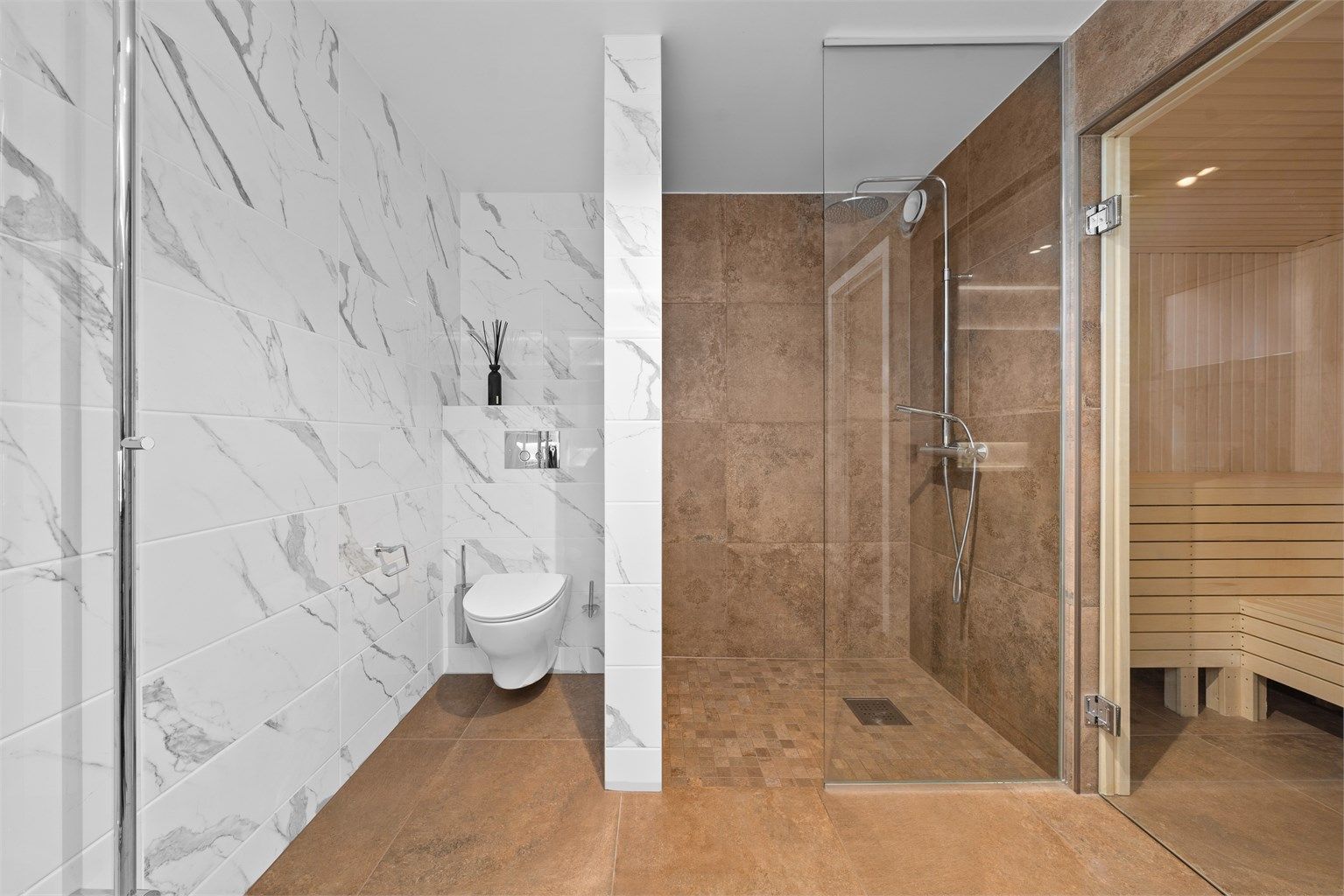 Dusjnisje med glassvegg, flislagt vegg med innebygd dusjhylle, og mosaikkfliser på gulv. Vegghengt toalett.