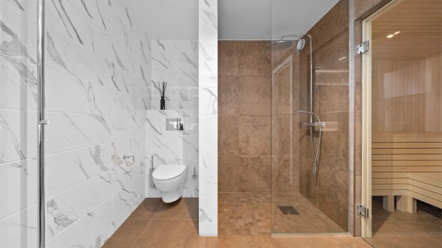 Dusjnisje med glassvegg, flislagt vegg med innebygd dusjhylle, og mosaikkfliser på gulv. Vegghengt toalett.