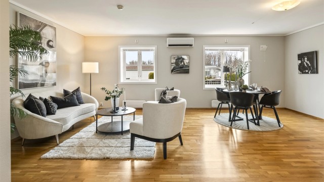 En lys og lettmøblert stue med gjennomgående parkett og god plass til både sofagruppe og spisebord.