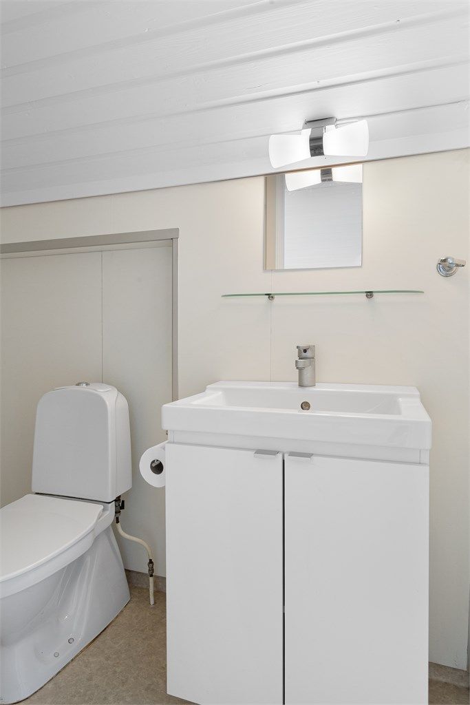 Badet i loftsleiligheten har gulvbelegg, våtromsplater på veggene og vegghengt servantskap.