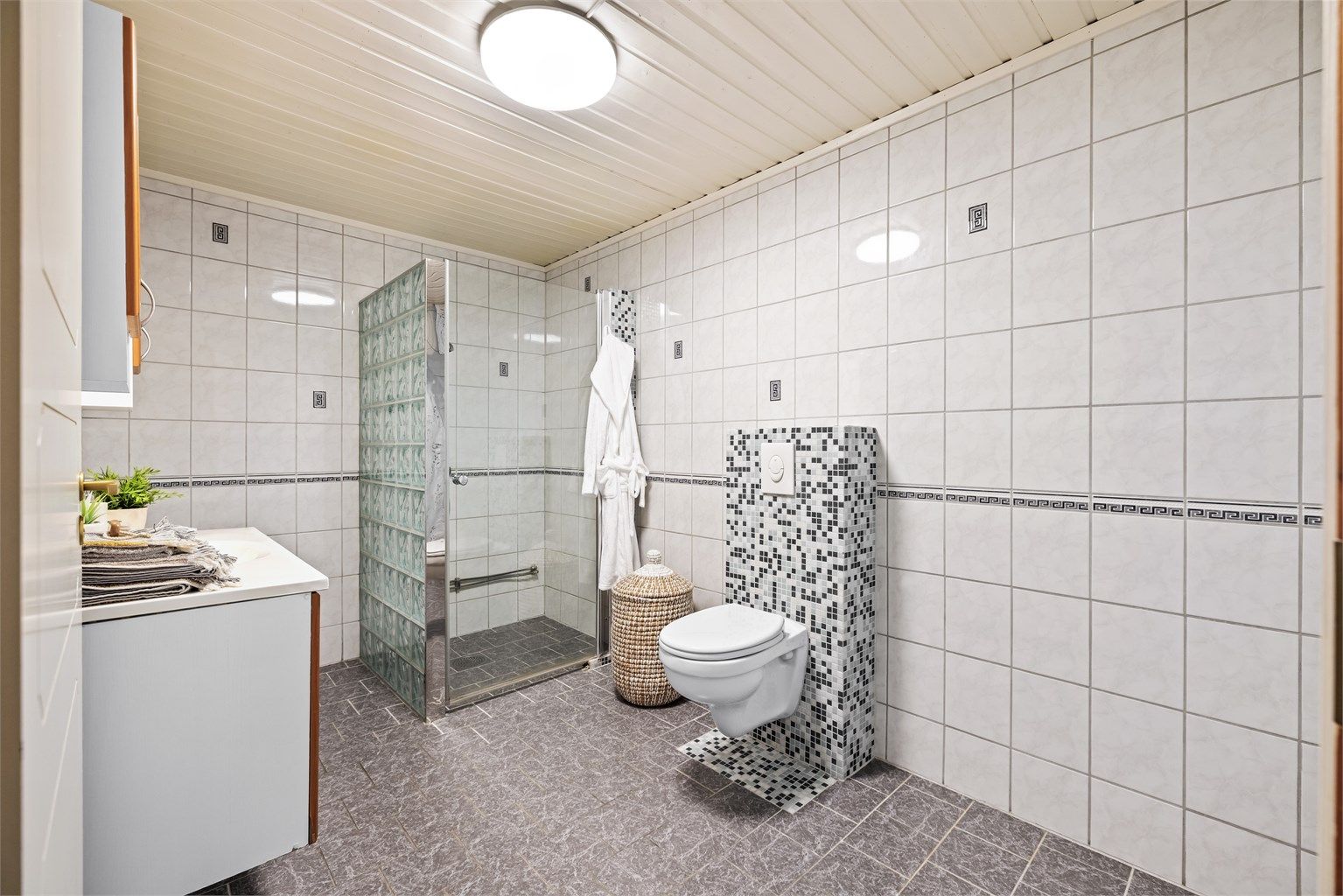 Dusjhjørne med vegger i glassbyggerstein og glassdør, samt vegghengt toalett.