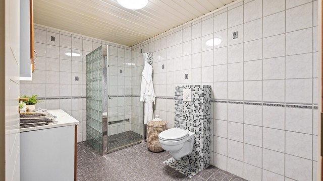 Dusjhjørne med vegger i glassbyggerstein og glassdør, samt vegghengt toalett.