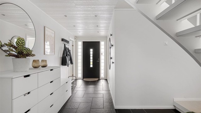 Romslig gang med fliser på gulv og varmekabler. Rikelig med plass til å sette av sko og henge av yttertøy. Spotter i tak.