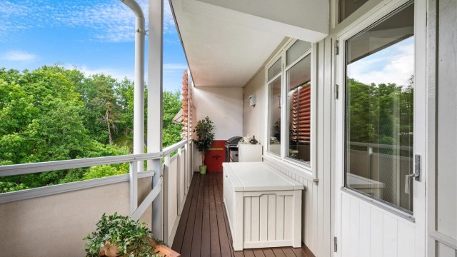 Verandaen strekker seg langs leilighetens fasade og har gulv belagt med terrassebord.