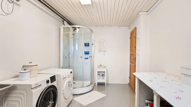 Praktisk vaskerom med elektrisk gulvvarme, dusjkabinett og opplegg for vaskemaskin og tørketrommel.