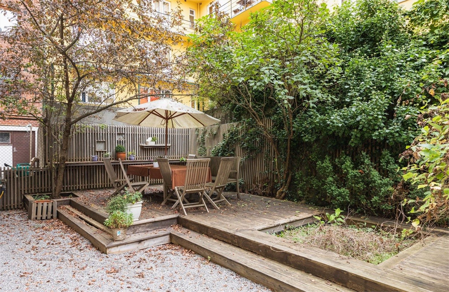 Avskjermet bakgård med beplantning, grusede arealer og terrasseplatting i trykkimpregnert virke.