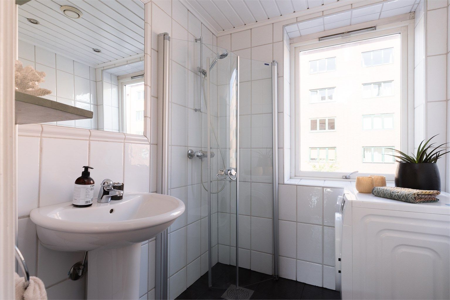 Et tidløst, flislagt bad med elektrisk gulvvarme og opplegg for vaskemaskin.