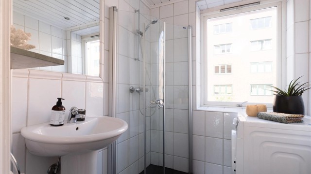 Et tidløst, flislagt bad med elektrisk gulvvarme og opplegg for vaskemaskin.