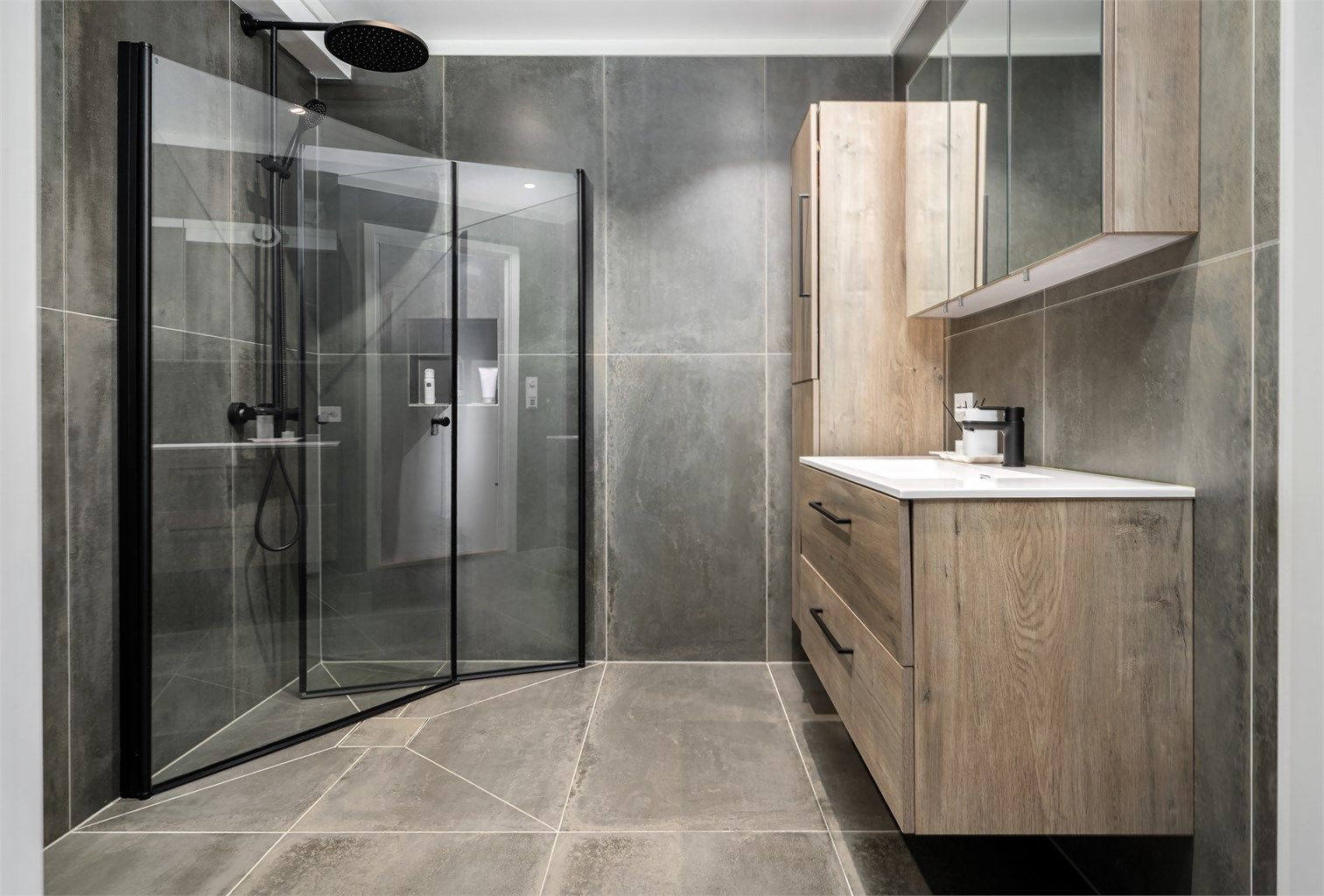 Et gjennomført og moderne baderom med store fliser og en romslig dusjsone med regnfallsdusj.