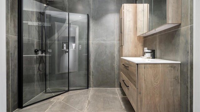 Et gjennomført og moderne baderom med store fliser og en romslig dusjsone med regnfallsdusj.
