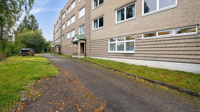 Teglsteinsfasade og asfaltert adkomstvei til oppgangen.