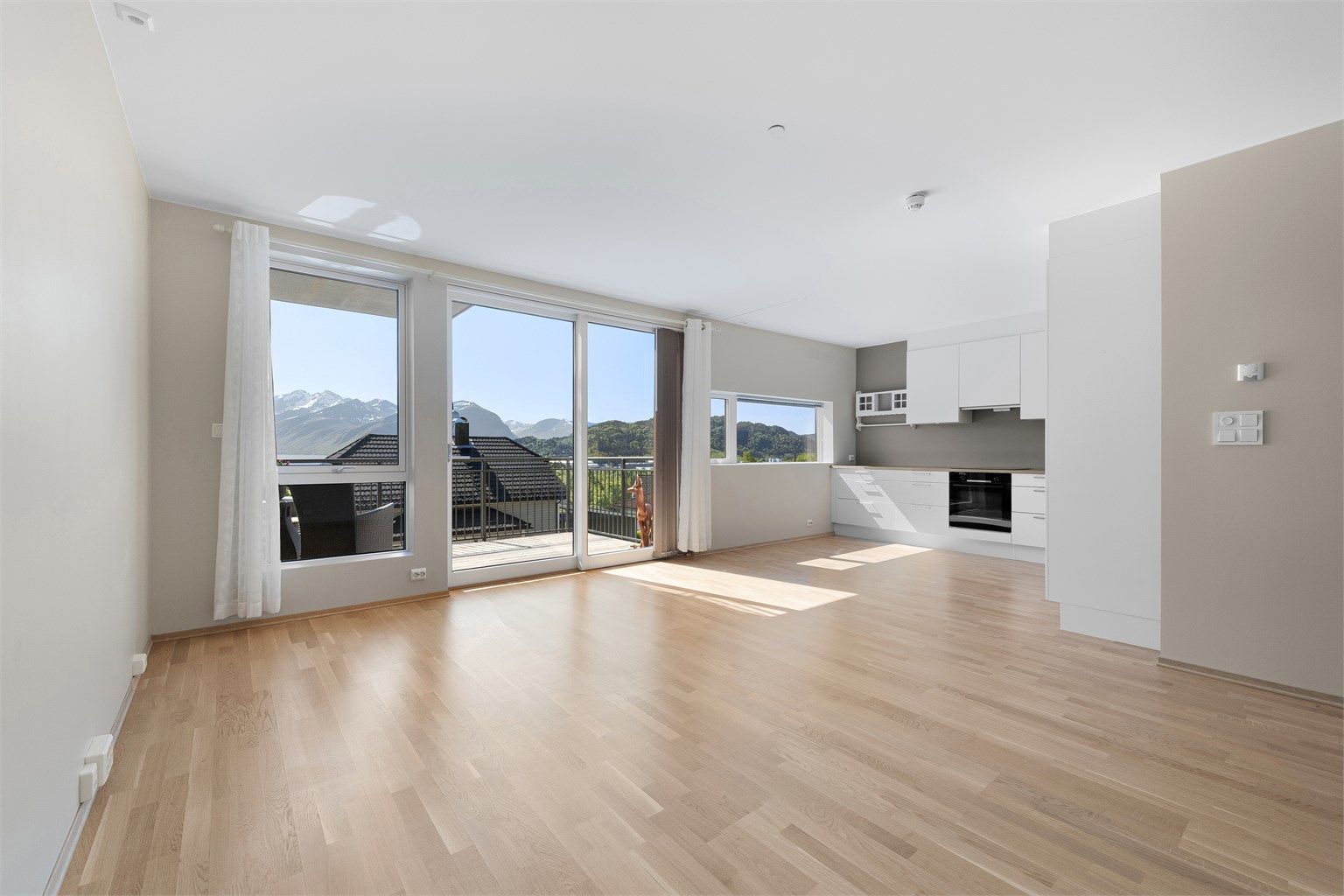 Stue og kjøkken i åpen løsning med lyse overflater og listefrie overganger mellom vegger og tak