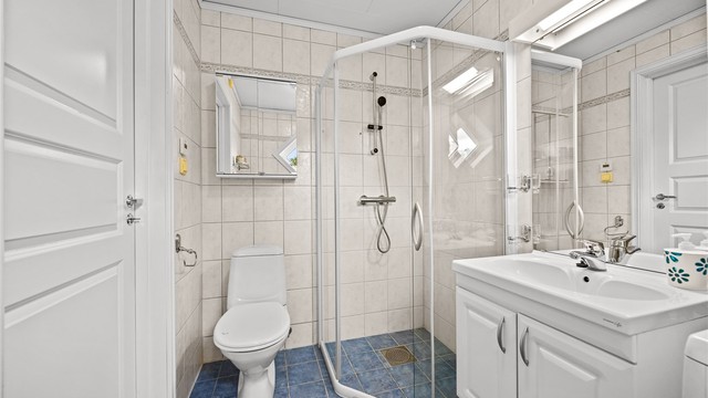 Badet er utstyrt med vegghengt servantskap, overskap med speil og gulvmontert toalett.
