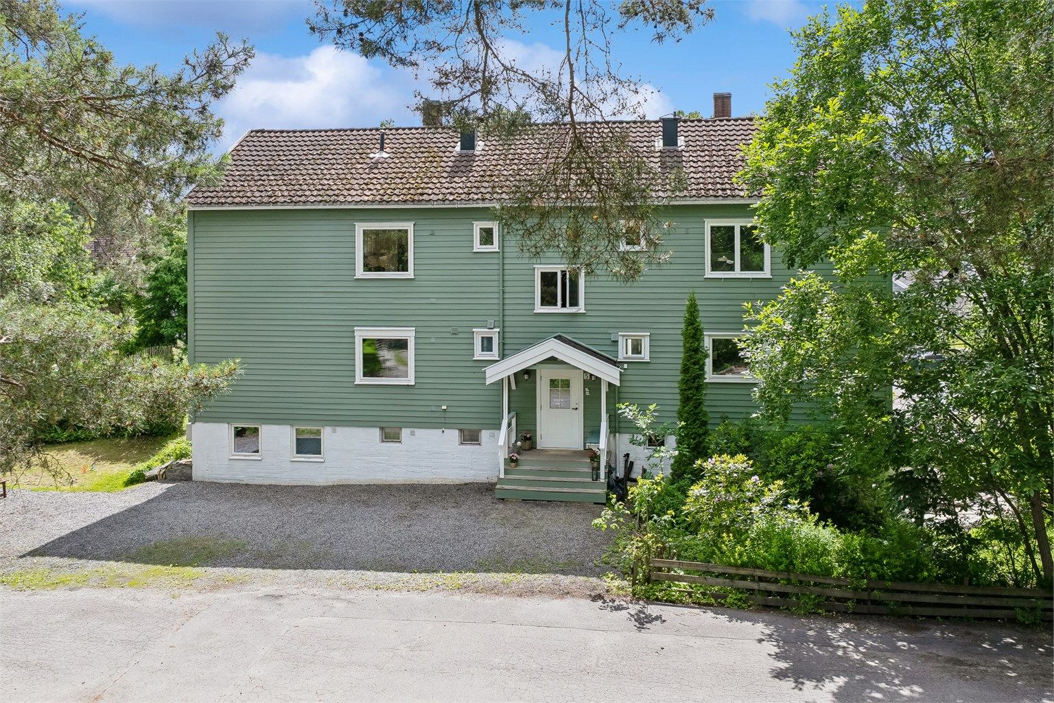 Fasade med inngangsparti og flere biloppstillingsplasser.