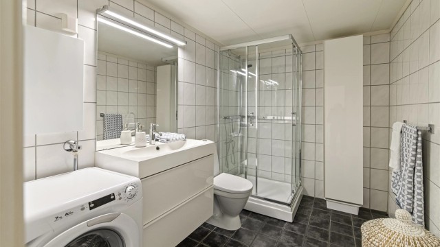 Pent flislagt bad fra ca. 2010 med varmekabler i gulvet. Det er montert innredning med slette fronter, heldekkende servant og ett greps armatur. Speil, overlys og stikkontakt. Dusjkabinett og gulvstående toalett. Badet har også opplegg til vaskemaskin.