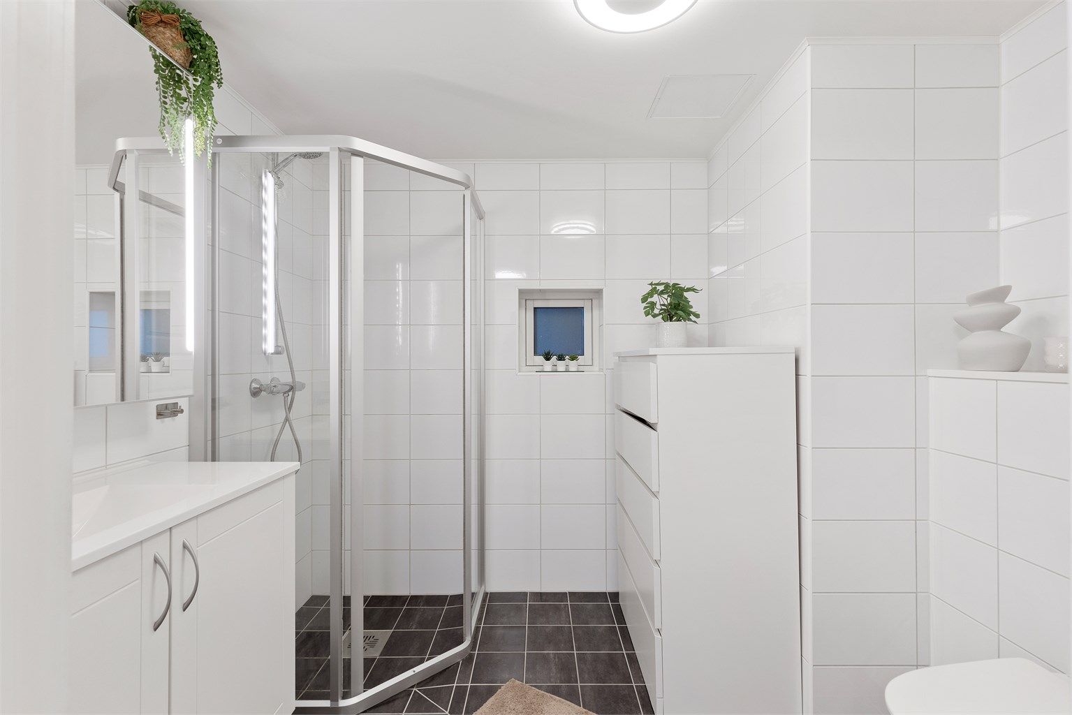 Videre er badet innredet med servantskap med speil og lys, vegghengt toalett og dusjhjørne. 