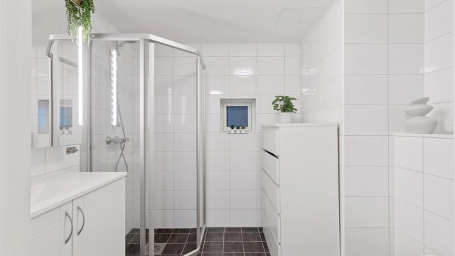Videre er badet innredet med servantskap med speil og lys, vegghengt toalett og dusjhjørne.