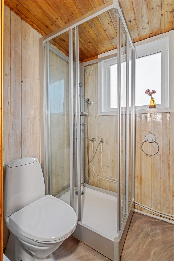 Badet er innredet med dusjkabinett, gulvstående toalett og panelbord på vegger.