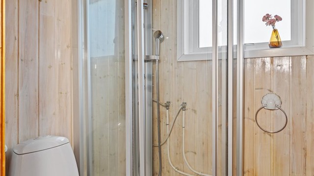 Badet er innredet med dusjkabinett, gulvstående toalett og panelbord på vegger.