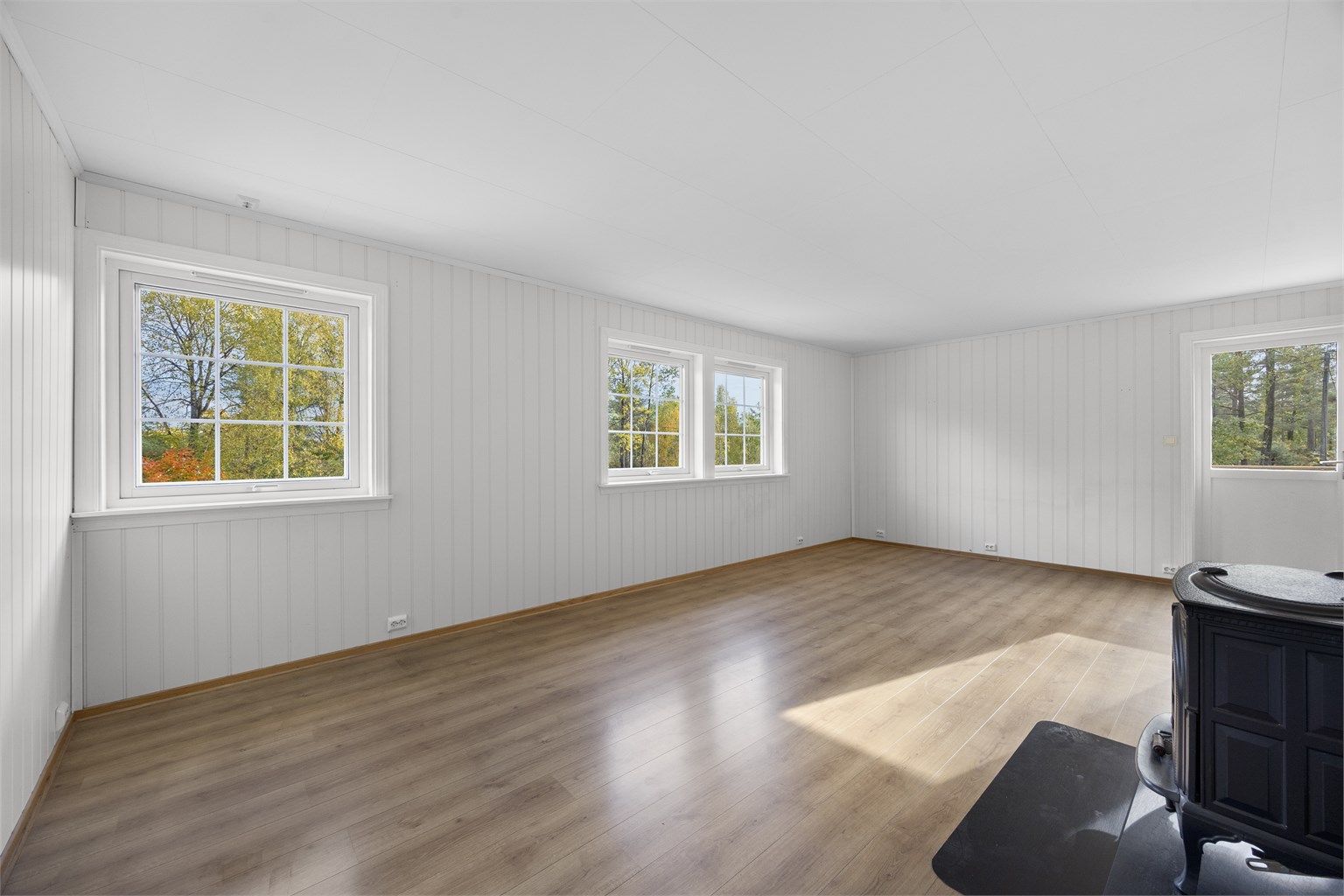 Lys stue med hvitmalt trepanel og god plass til både sofagruppe og spisebord.