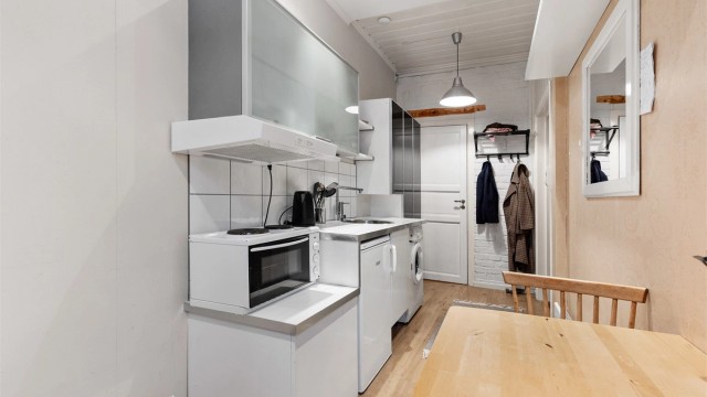 Åpen kjøkkenløsning. Innredningen er fra ukjent årstall med slette fronter. Benkeplate av laminat. Nedfelt oppvaskkum med ett-greps kjøkkenarmatur. Benkeskapsbelysning og stikkontakter over kjøkkenbenk. Frittstående kjøleskap. Ventilator i overskap.