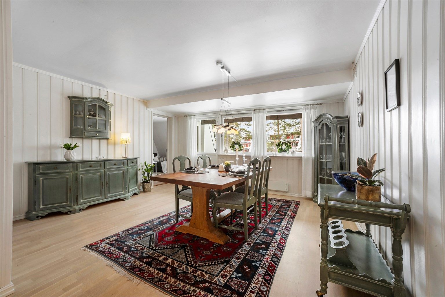 Spisestuen har lys parkett på gulvet og hvitmalt panel på veggene.