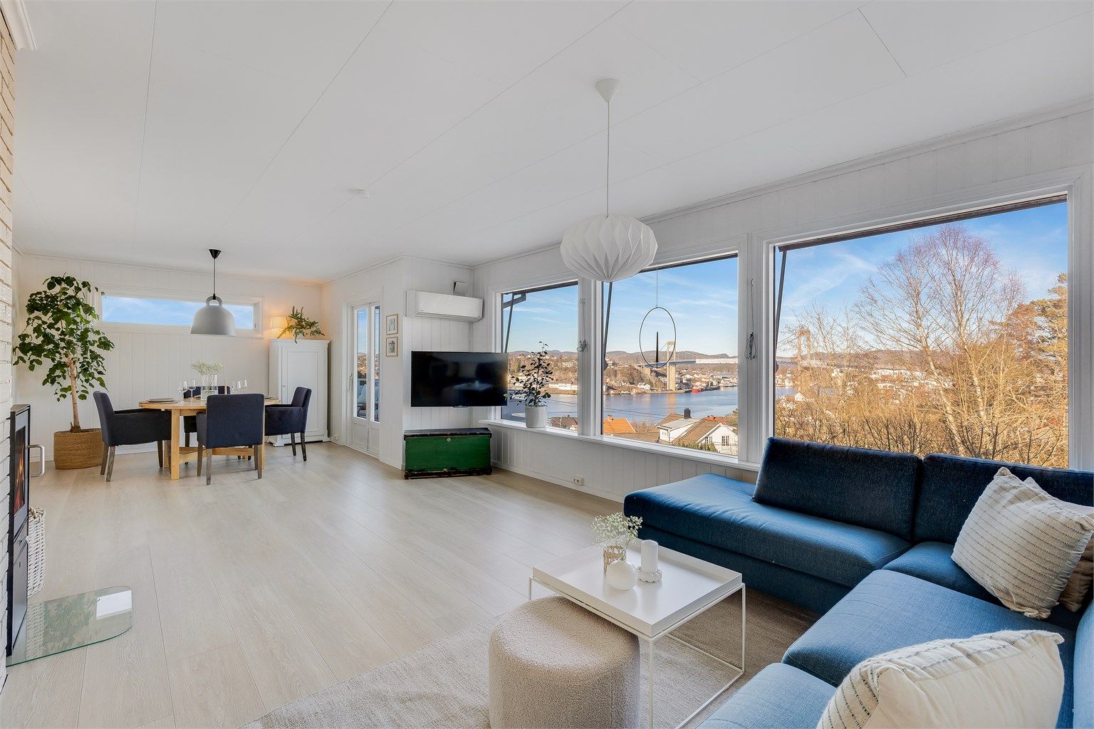 STUEN ER LYS og åpen. de store vinduene slipper inn rikelig med naturlig lys. Et tre i hjørnet bak spisegruppen gir god atmosfære i rommet.