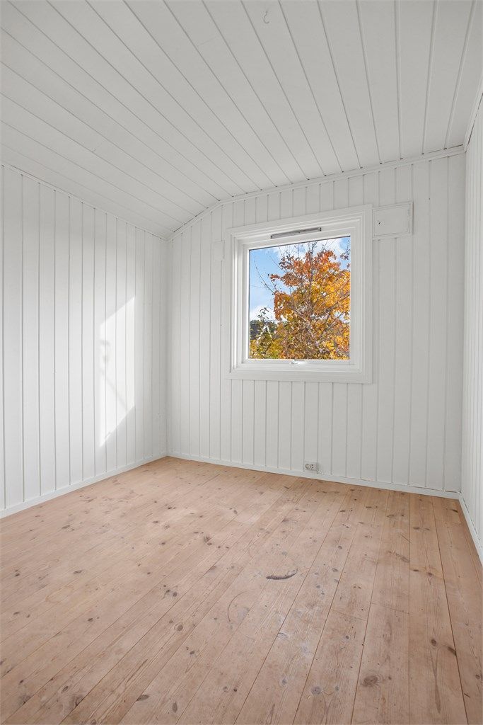 Soverom med tregulv og hvitmalte panelvegger.