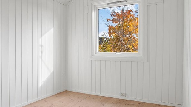 Soverom med tregulv og hvitmalte panelvegger.