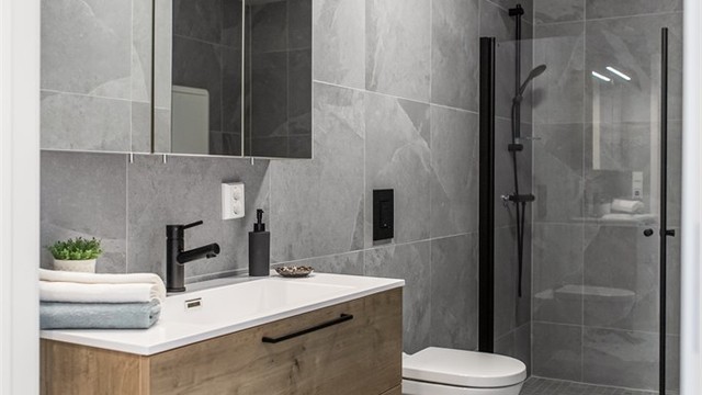 Badet er innredet med vegghengt toalett, servant med skuffeseksjon og speilskap samt dusjhjørne