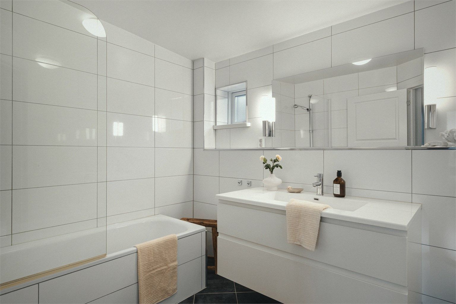 Helfliset bad med varmekabler fra byggeår som er innredet med baderomsmøbler, badekar med dusjvegg og vegghengt wc