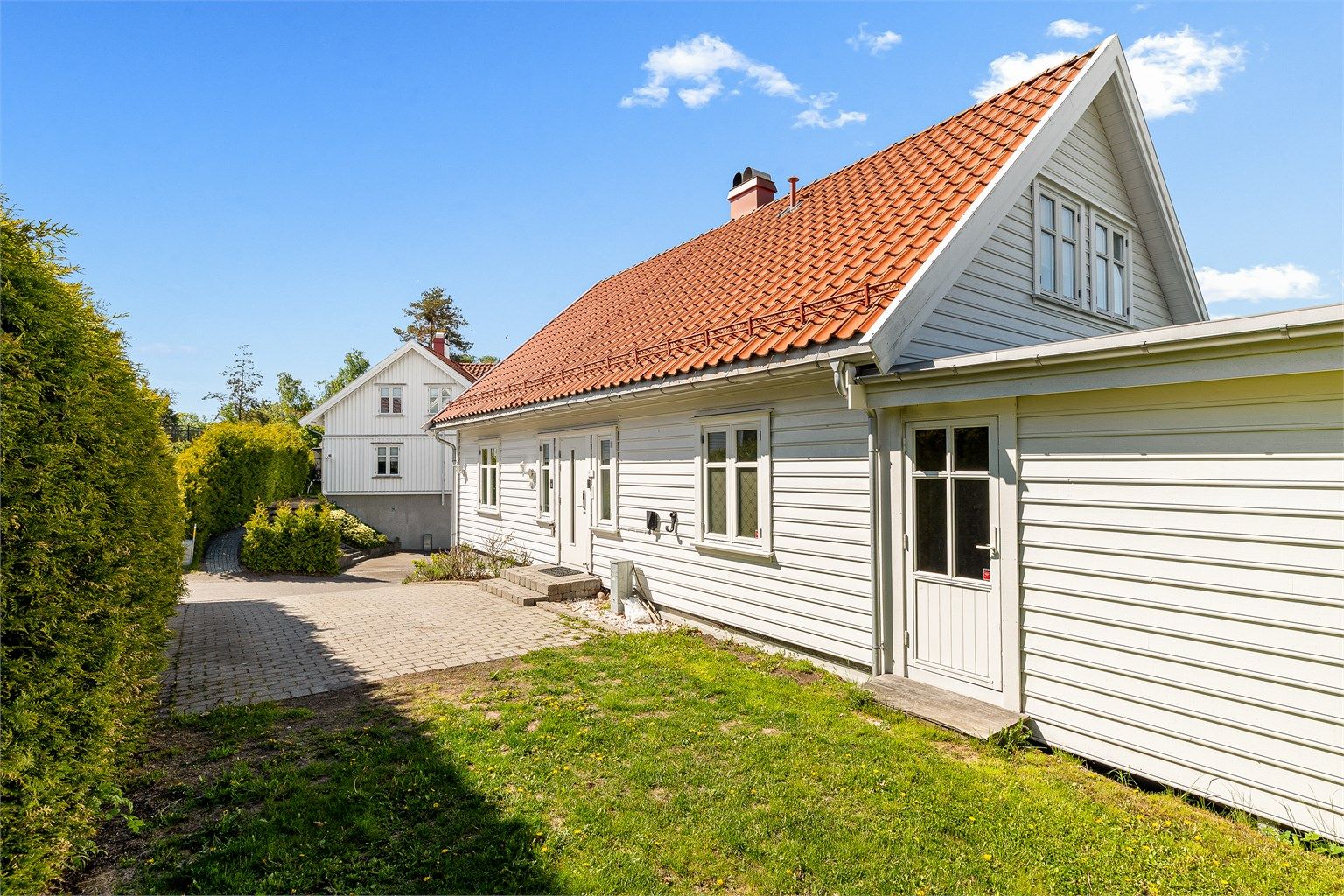 Eiendommen ligger på en skrånende tomt som er opparbeidet med plen og beplantning. Dør til høyre er inn til utestuen.