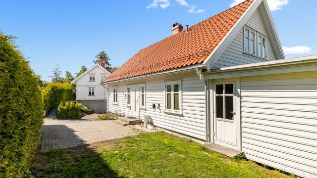Eiendommen ligger på en skrånende tomt som er opparbeidet med plen og beplantning. Dør til høyre er inn til utestuen.