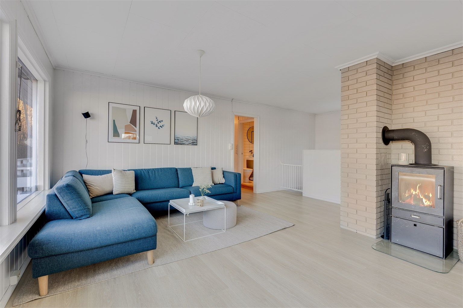 Sofaen vender mot de store stuevinduene med utsikt utover sjøen og mot peisovnen.