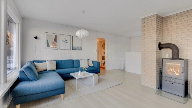 Sofaen vender mot de store stuevinduene med utsikt utover sjøen og mot peisovnen.