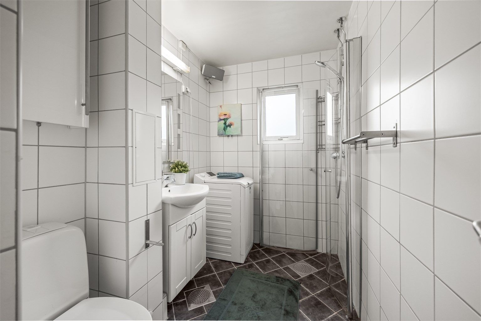 Badet er utstyrt med dusjhjørne med innfellbare dører og opplegg for vaskemaskin. Varme i gulvene