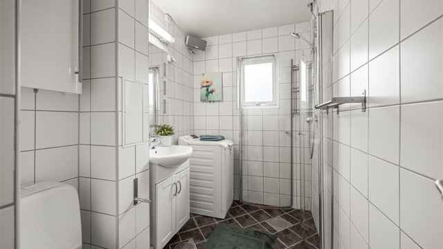 Badet er utstyrt med dusjhjørne med innfellbare dører og opplegg for vaskemaskin. Varme i gulvene