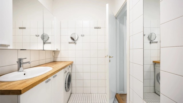 Videre er det overskap med speildører og stikkontakt på vegg over benkeplate. Det er opplegg for vaskemaskin.
